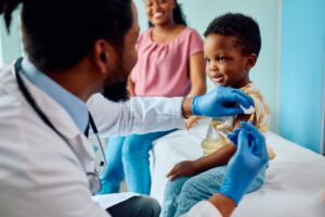 A male pediatrician giving a young, happy boy his vaccines as the boy's mom smiles in the background