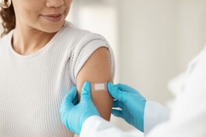 A woman smiling down at her upper arm as a nurse places a band-aid over the spot she just got a flu vaccine